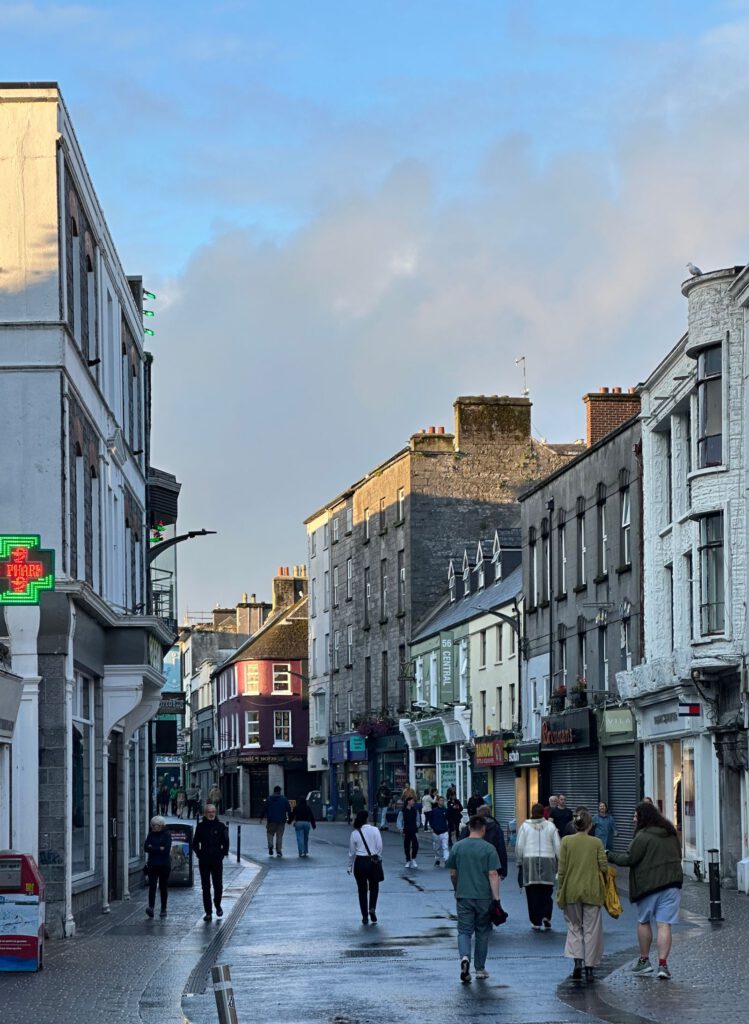 Historische Straße in Galway mit bunten Läden und Menschen auf nassem Pflaster